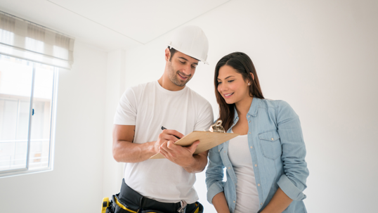 Construction worker and woman looking at clip board with construction plans both looking at ease
